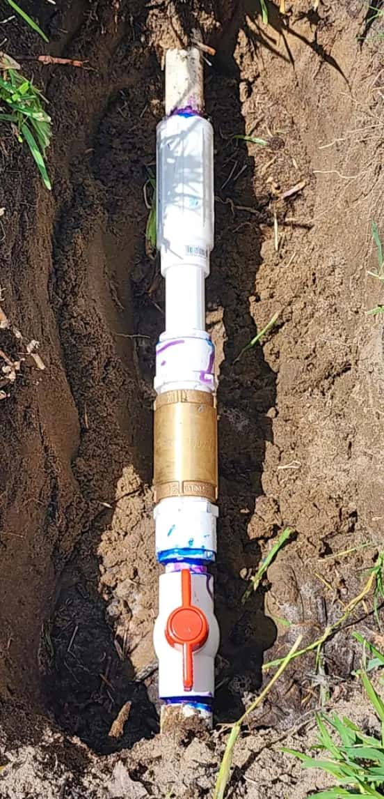 Repaired irrigation mainline in an open trench with a new brass fitting and shut-off valve