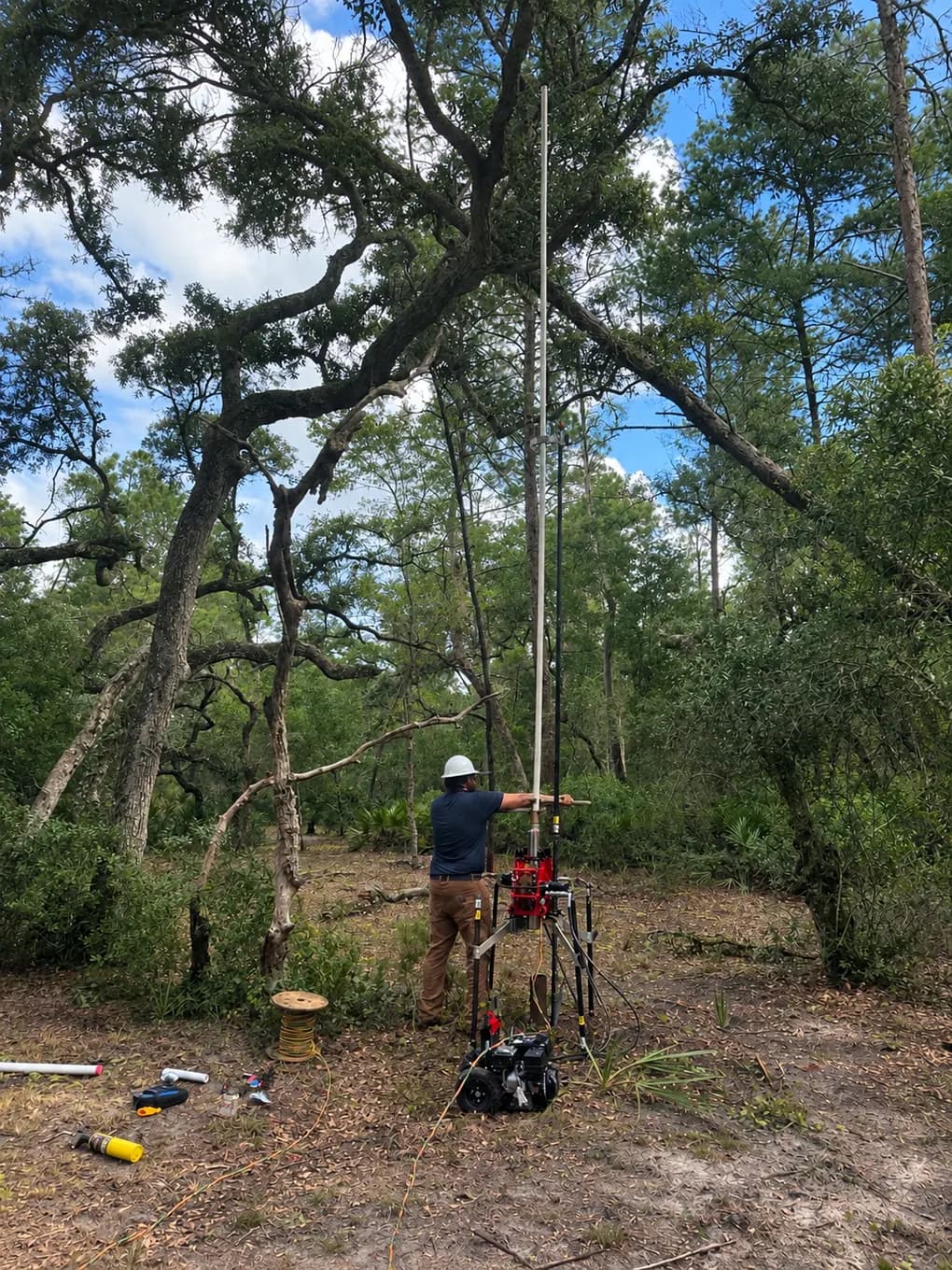 IrriGators LLC technician running a hydraulic pump hoist to pull a well pump in a wooded lot