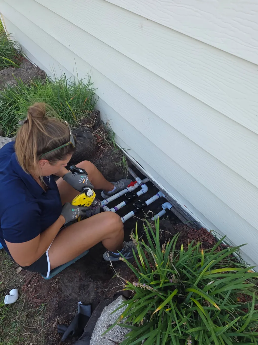 IrriGators LLC technician building a sprinkler valve manifold beside a home