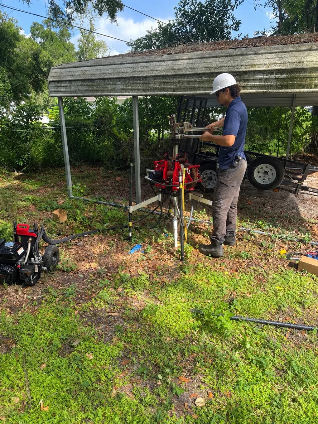 IrriGators LLC technician working a hydraulic well pump hoist beside a carport