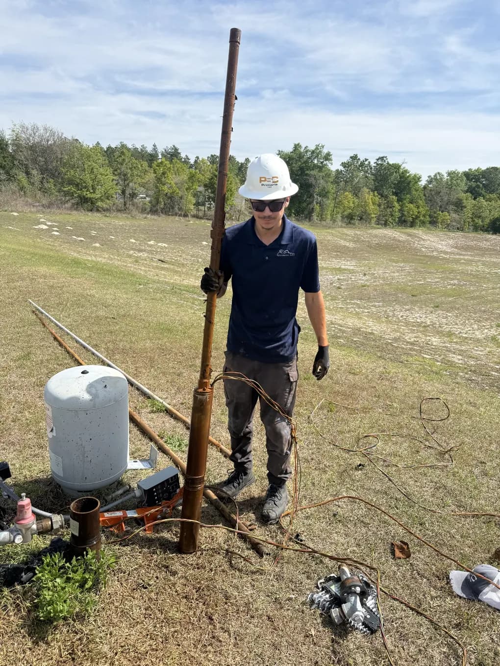 IrriGators LLC well technician standing with pulled galvanized drop pipe beside a new pressure tank