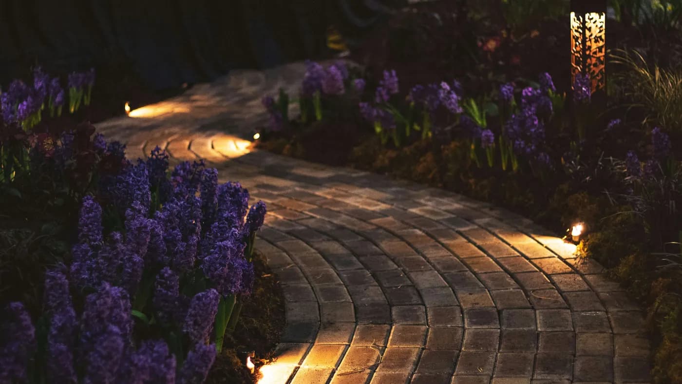 Low voltage landscape lighting along a curved paver walkway lined with flowering beds