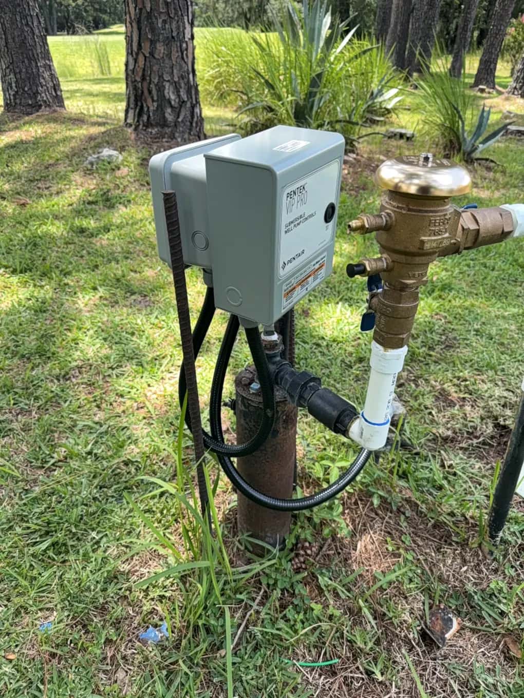 Pentek VIP Pro submersible well pump controller mounted on a well casing beside a backflow preventer